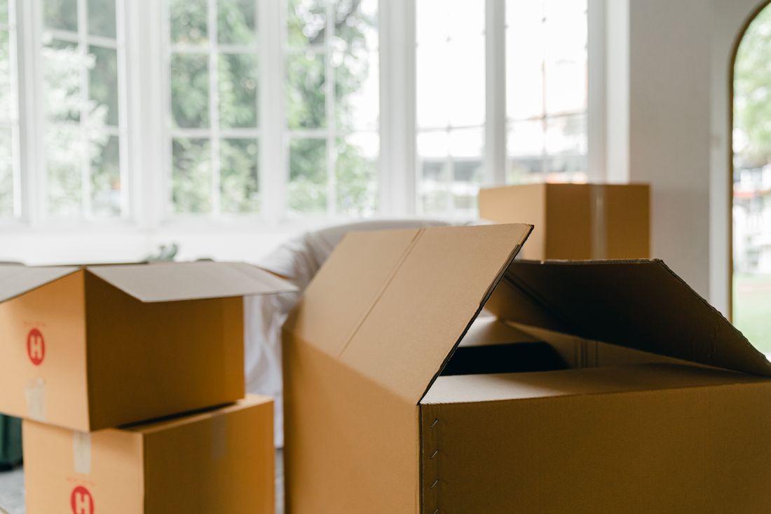 Open cardboard moving boxes standing in a bright empty room by a window