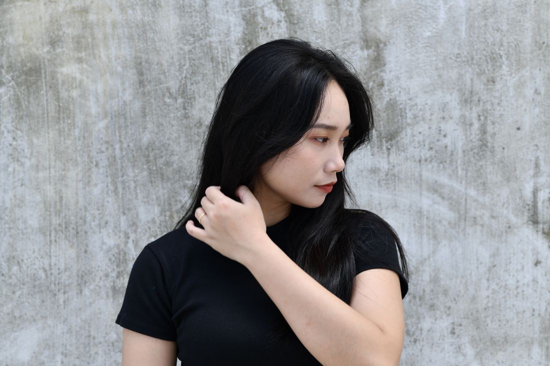 A person in a plain black top standing against a bare concrete wall in soft daylight