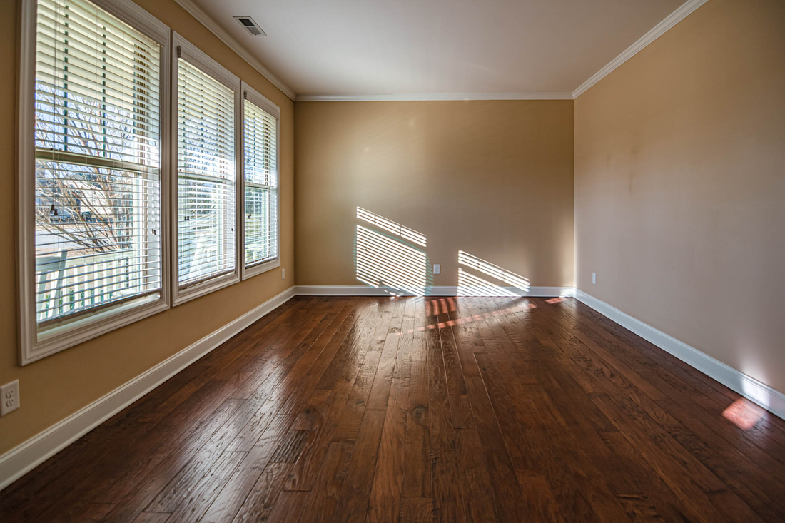 An empty room with wood floors and daylight coming through a bank of shuttered windows