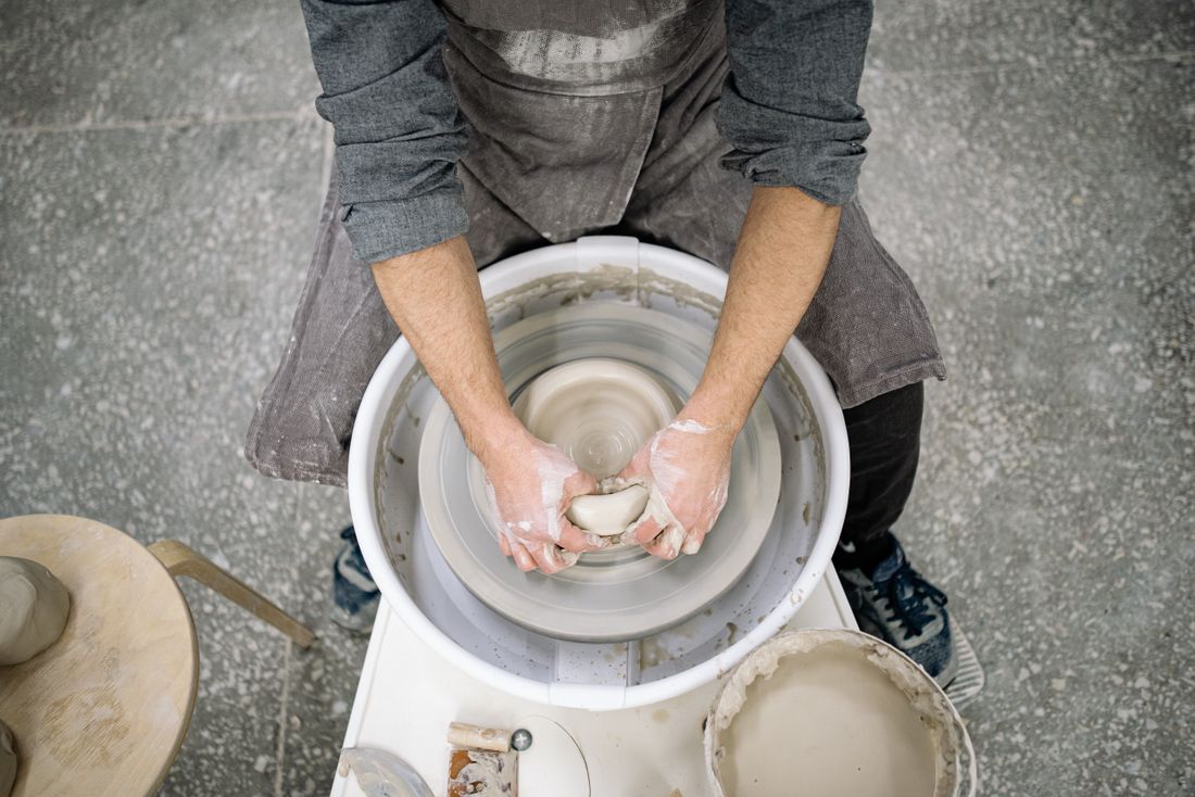 Overhead view of a person's hands shaping clay on a pottery wheel, apron and workroom floor visible, face out of frame.