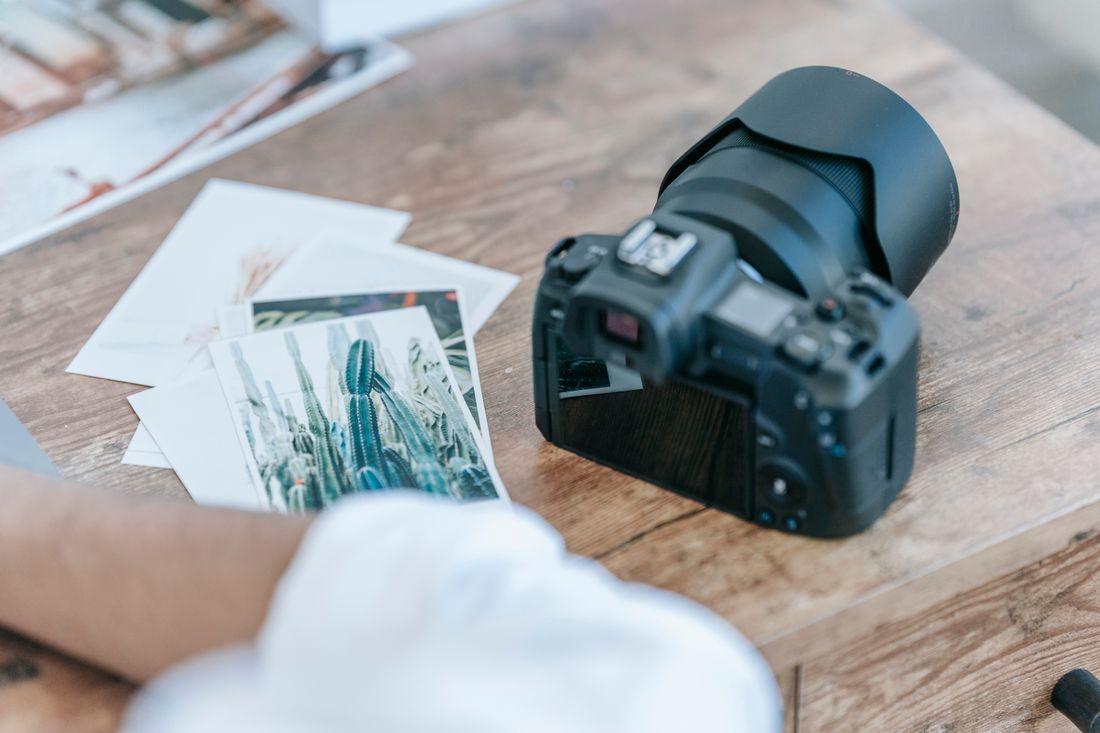 Camera and a small stack of printed photo prints on a wooden table, suggesting a photographer reviewing session output.