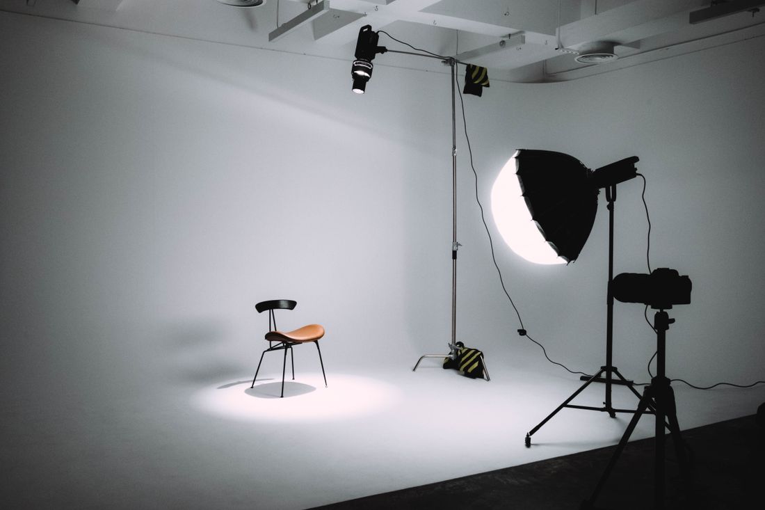 Empty photography studio with a single chair, softbox light, and plain backdrop set up for a portrait session.