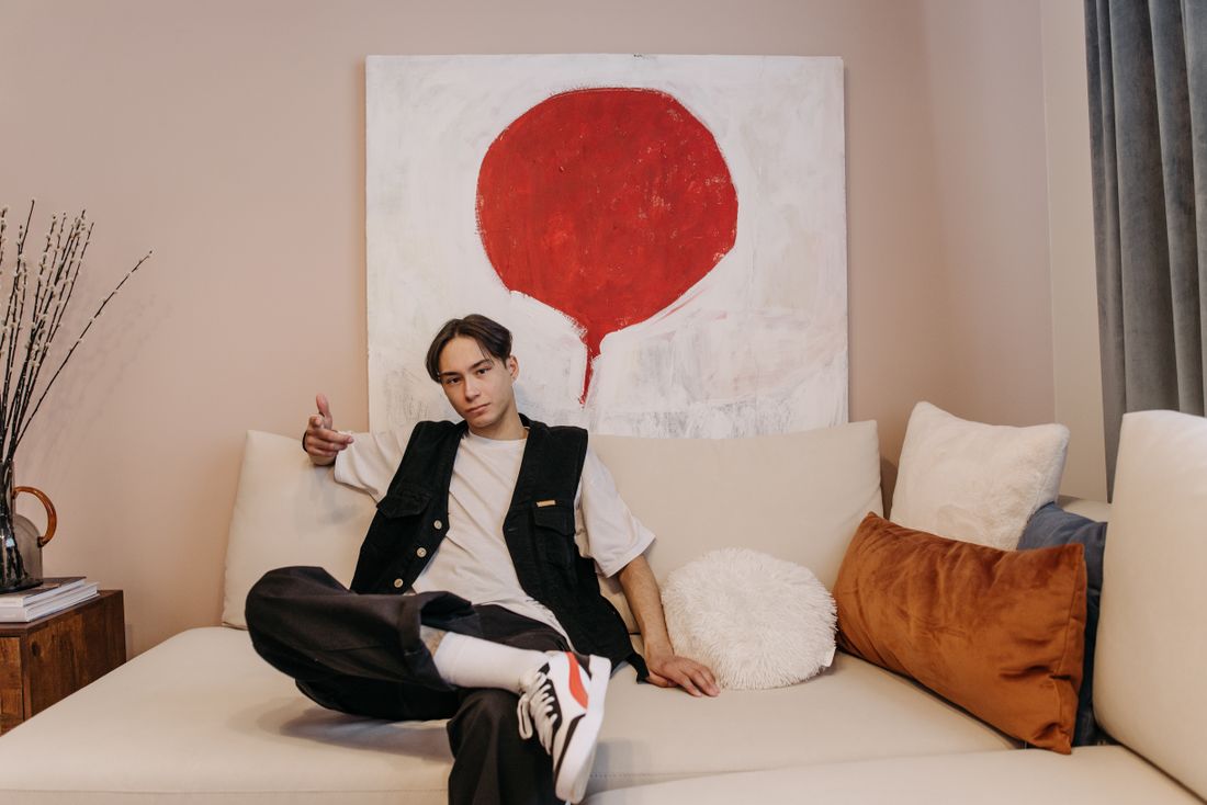 A man in casual clothing relaxes on a light sofa with a large abstract red circle painting on the wall behind him
