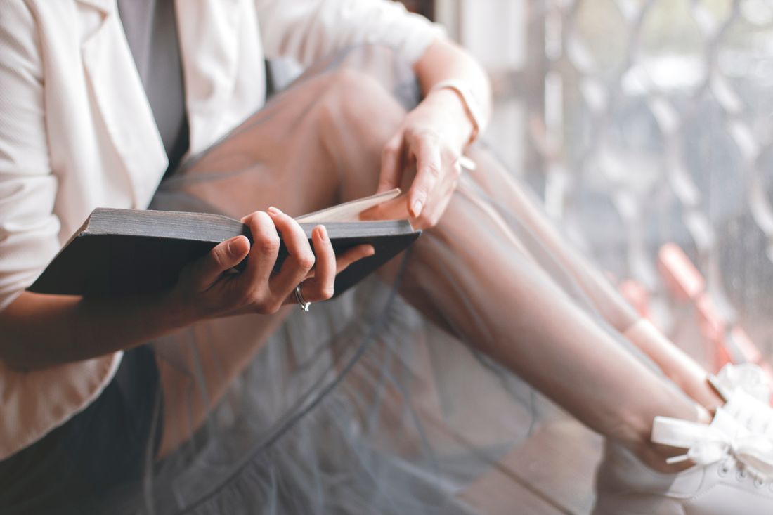 A person seated by a window holding a closed book with both hands, natural light, no visible text or screens