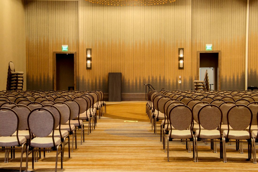 A plain, empty conference-style room with rows of chairs facing a podium, no signage visible