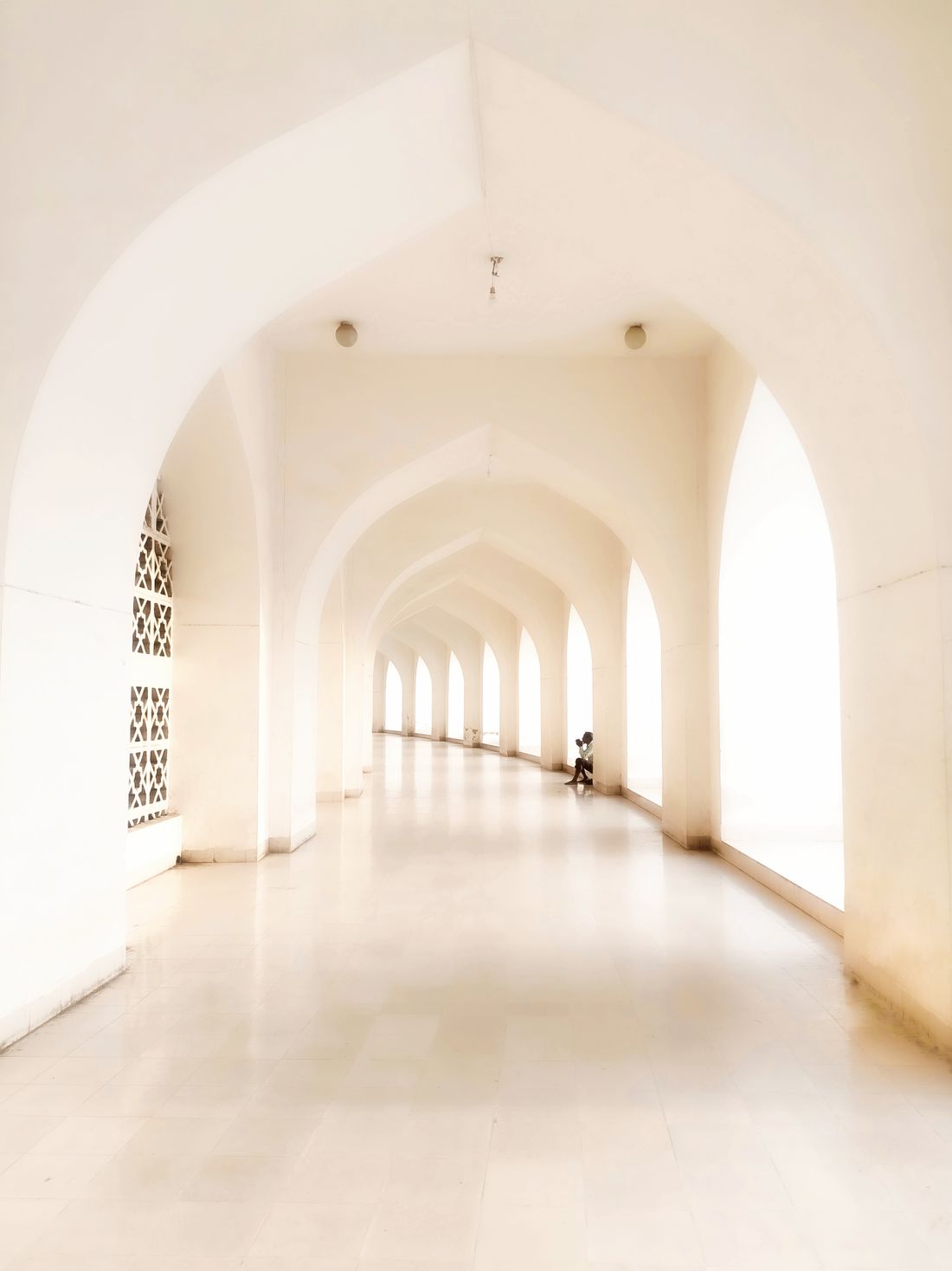 A bright, symmetrical white archway corridor stretching into the distance, empty except for one distant figure