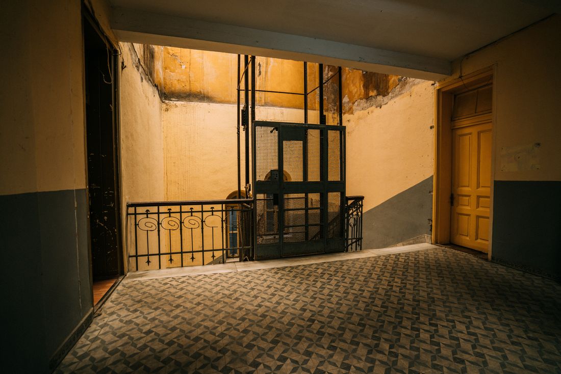A worn stairwell landing in an older building with an old caged freight elevator visible