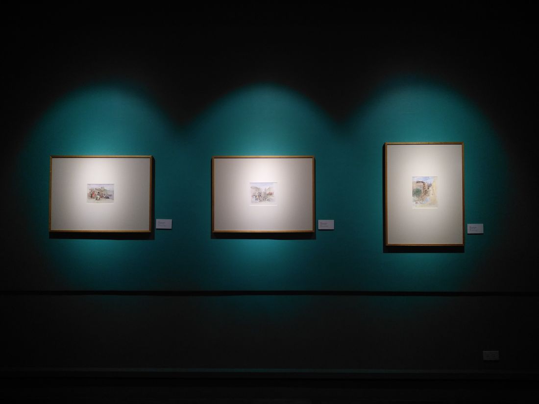 Three small framed artworks evenly lit on a quiet gallery wall with no visitors present