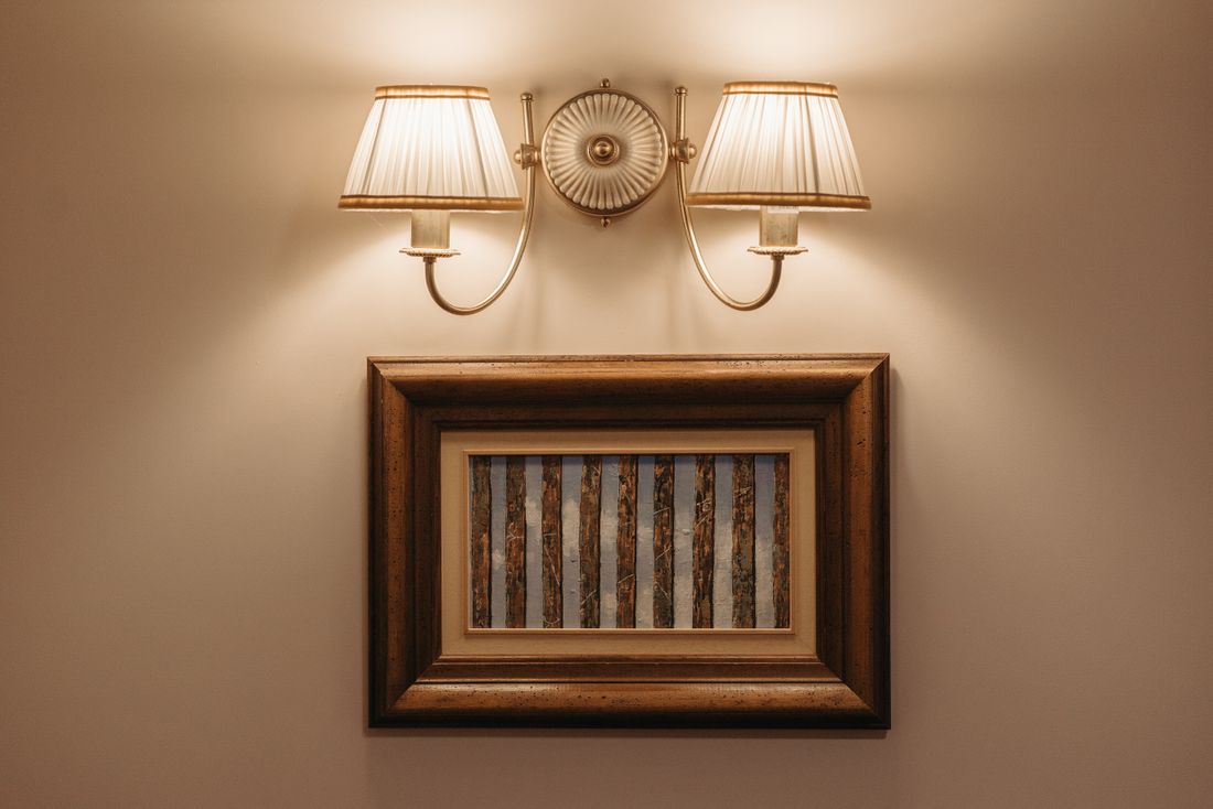 A framed piece of art lit by two wall sconces on a quiet, softly lit wall