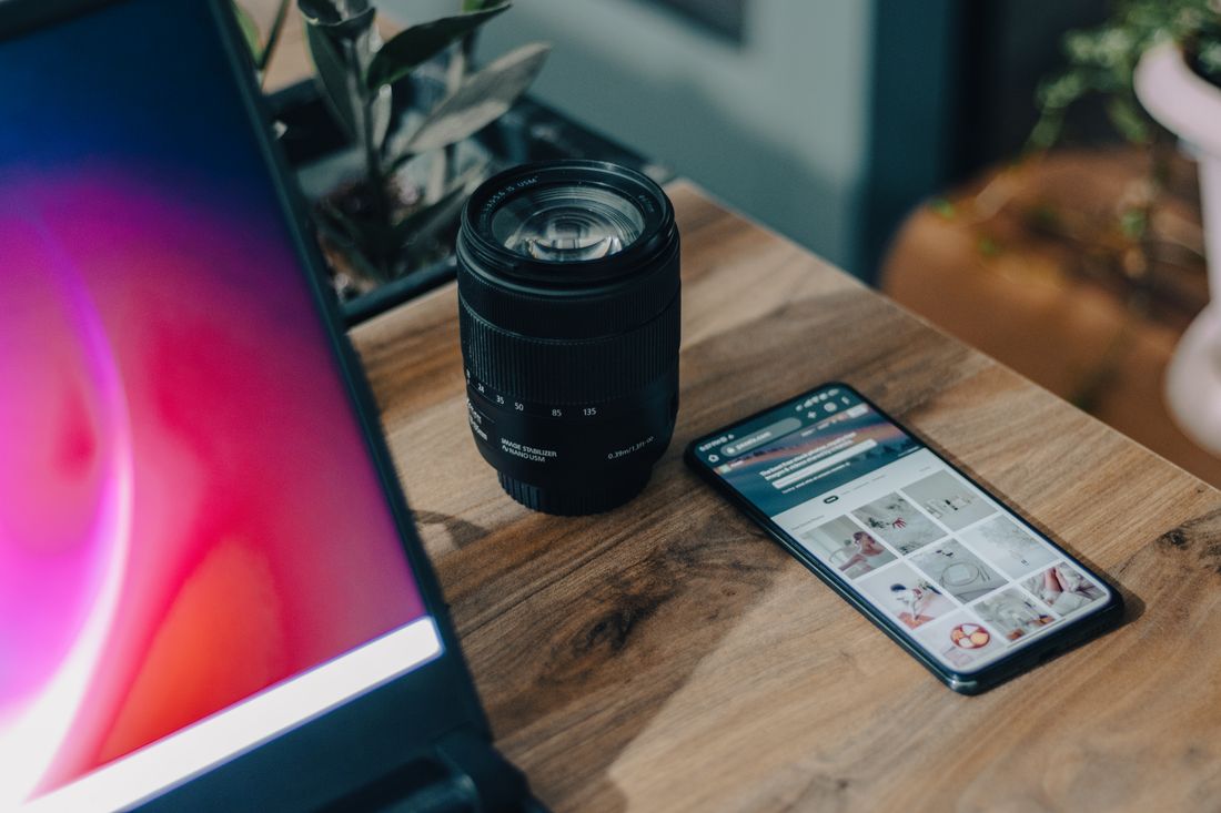 A camera lens and a smartphone resting side by side on a wooden desk