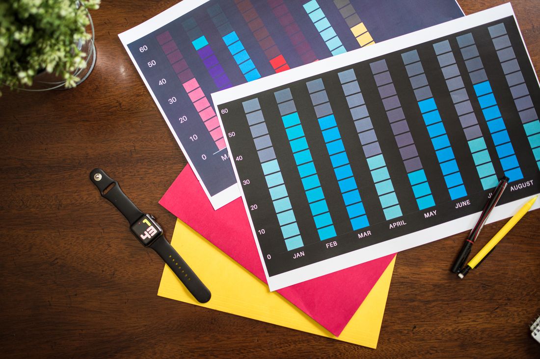 Printed colour swatch charts lying on a desk beside a pencil and a watch