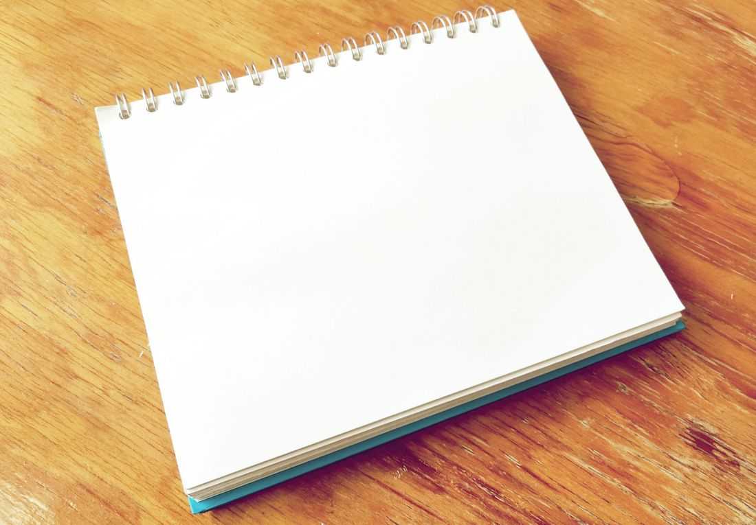 A spiral notebook with blank pages open on a wooden desk, photographed from an angle.