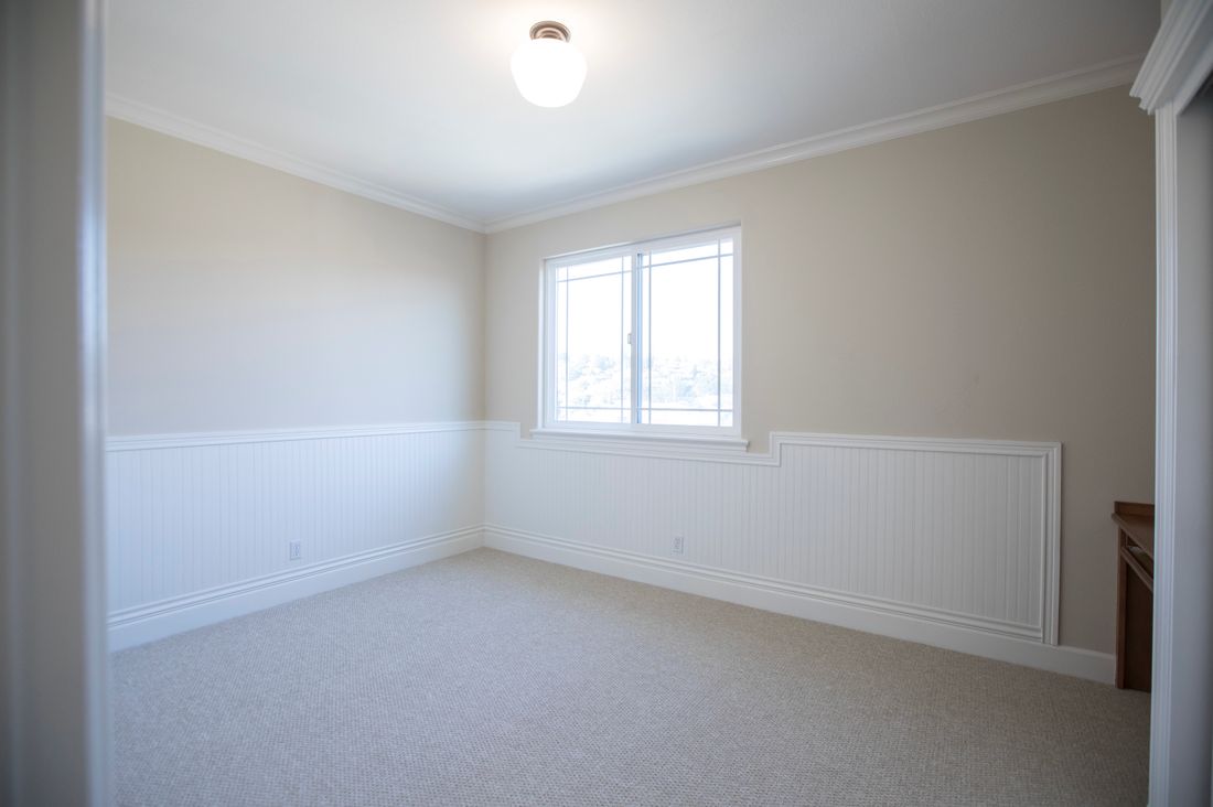 An empty, freshly prepared room with plain walls, a carpeted floor, and daylight from a window.