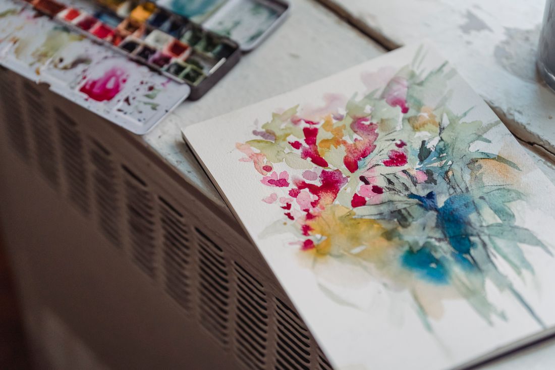 A watercolor painting on paper next to an open watercolor palette