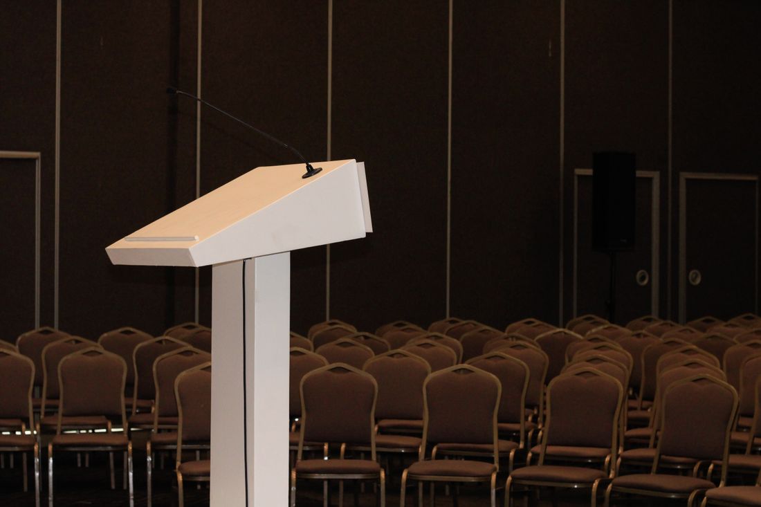 An empty conference room set up with a podium and rows of chairs before anyone has arrived.