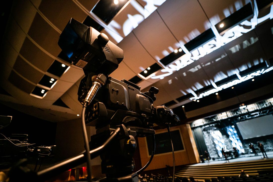 A professional video camera set up on a stand at the back of a modern indoor auditorium