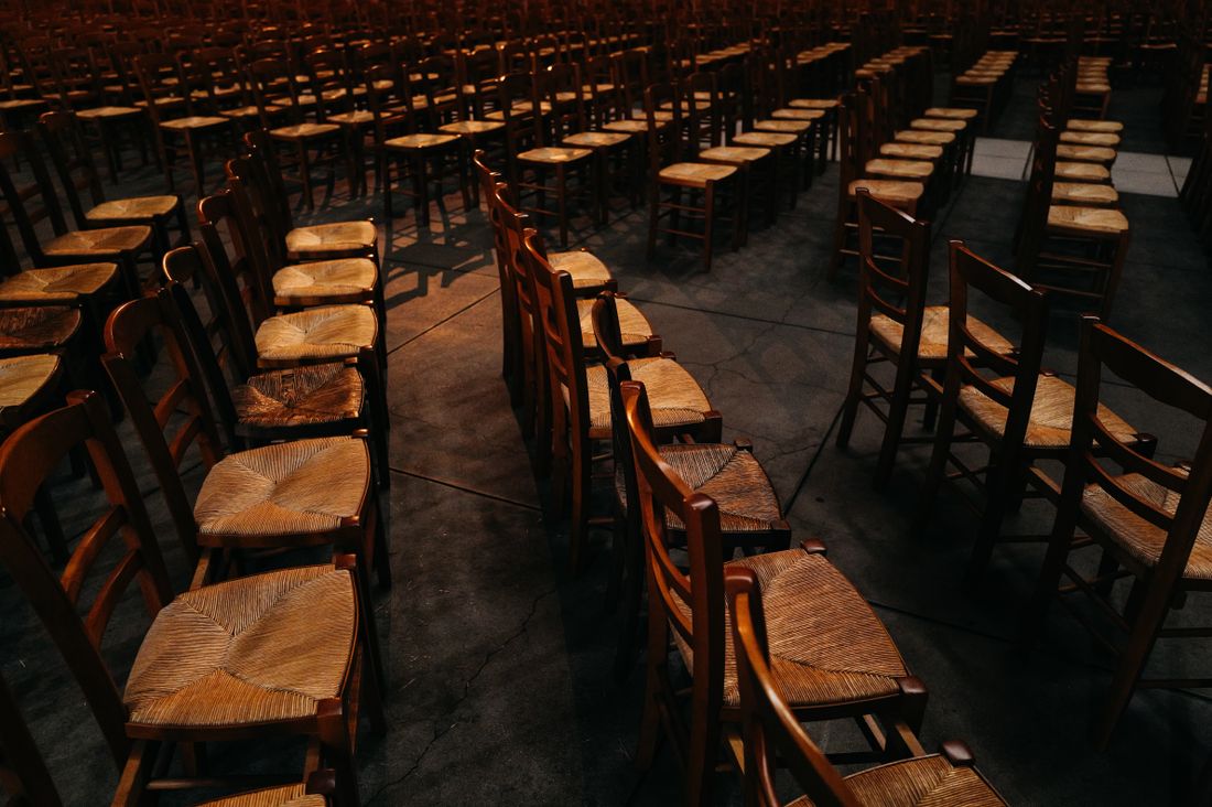 Rows of empty wooden chairs with woven seats catching warm low light in a large hall