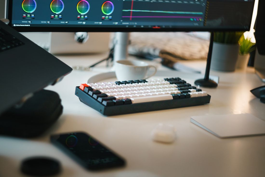 A video editing workspace with color grading wheels on a monitor and a keyboard on the desk
