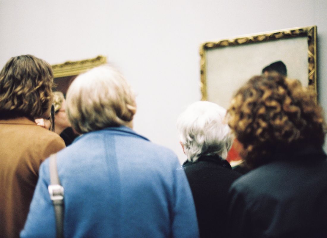 A tight cluster of people seen from behind, heads and shoulders close together, filling the space in front of a wall