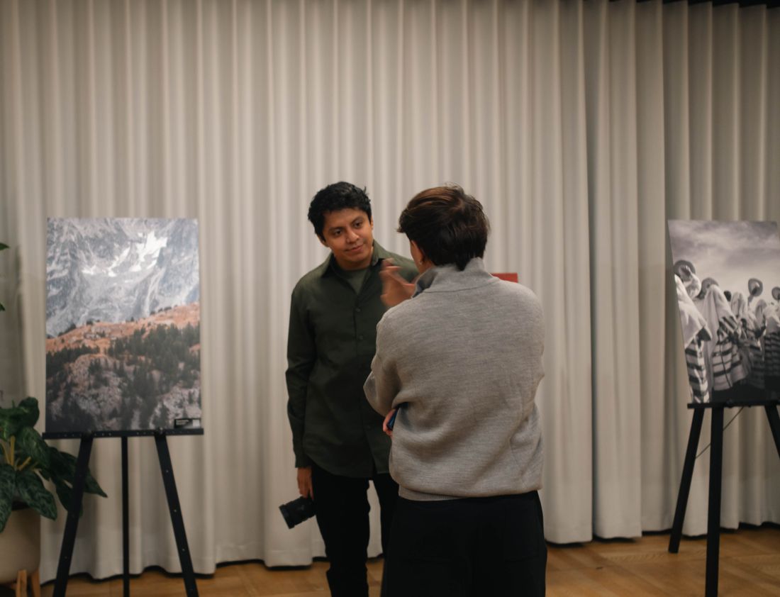 Two people in quiet conversation inside a small gallery with photographic prints on the wall