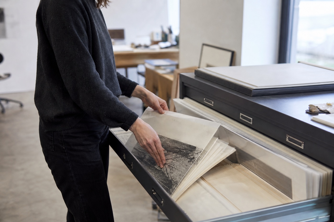 Artist organizing prints and protective sleeves in a modern flat-file archive cabinet