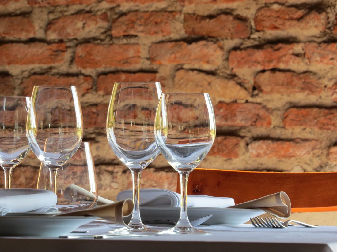 A row of clean empty wine glasses and folded napkins set on a table against a plain brick wall, no people present