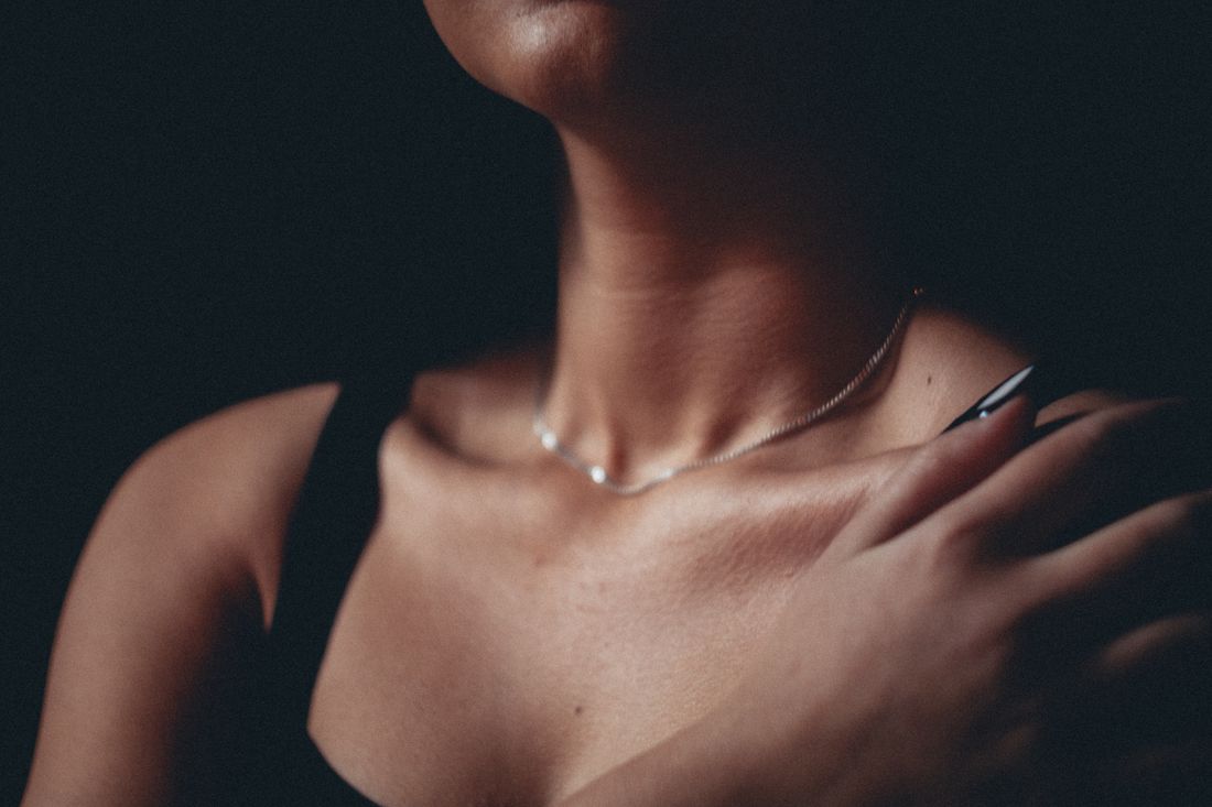 Close view of a person wearing a thin necklace and black top, with one hand resting near the shoulder.