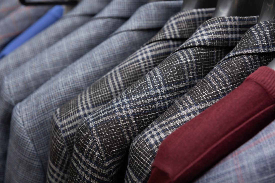 A row of tailored suit jackets in muted grey and navy patterns hung close together on a rail, photographed at an angle