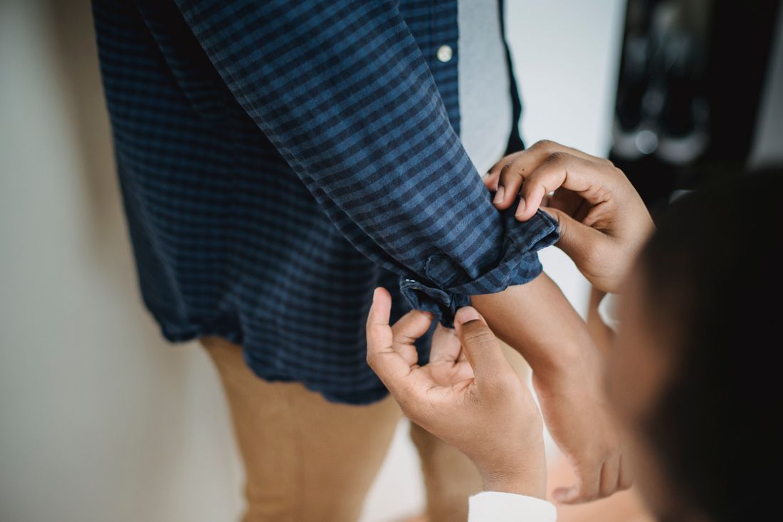 Close-up of hands adjusting the rolled cuff of a checkered shirt sleeve on someone else, both faces out of frame.