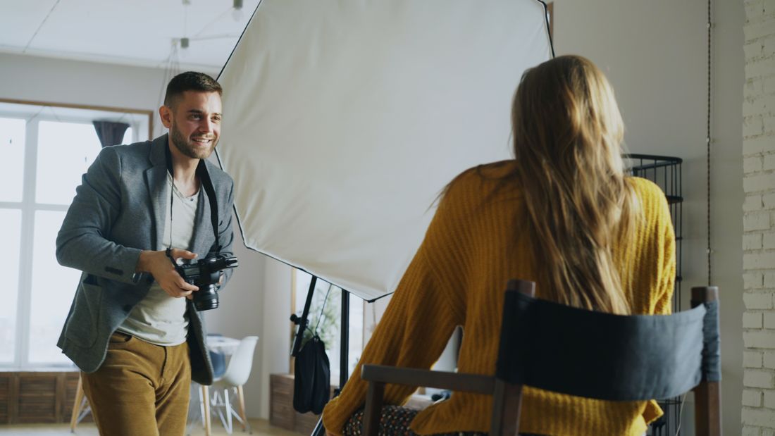 A photographer adjusting studio lighting while photographing a seated subject during an indoor portrait session