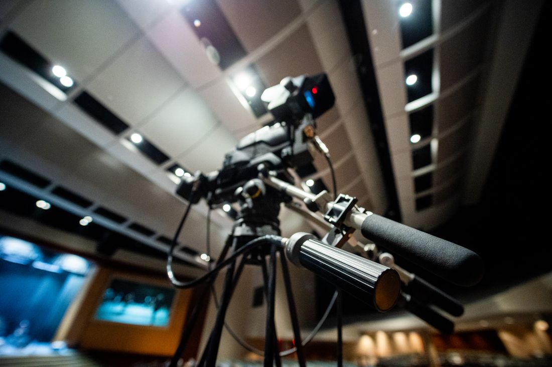 A professional video camera mounted on a tripod in a studio, seen from a low angle