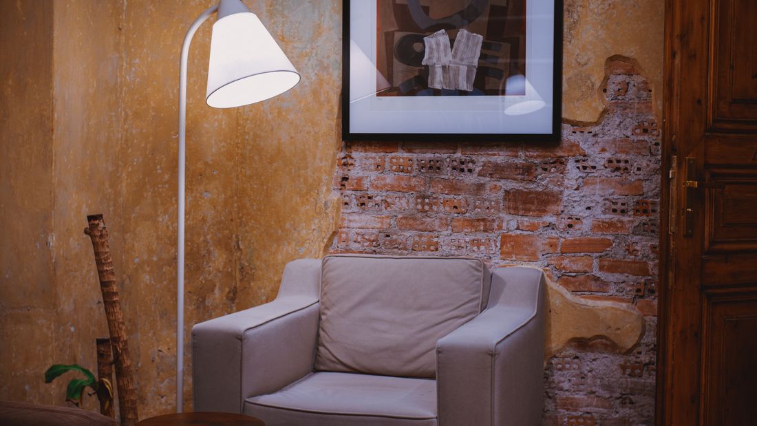 A single framed abstract painting hanging on a textured plaster and brick wall above an armchair and floor lamp