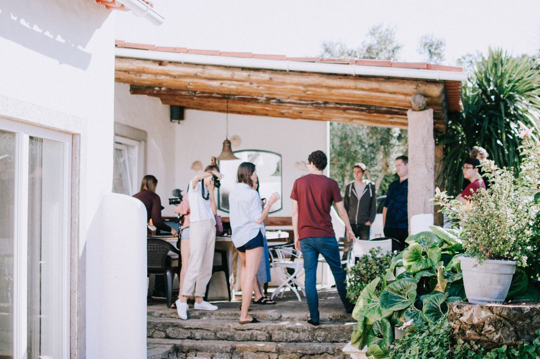 Guests mingling under a wood-beamed covered porch that opens onto garden steps in daylight