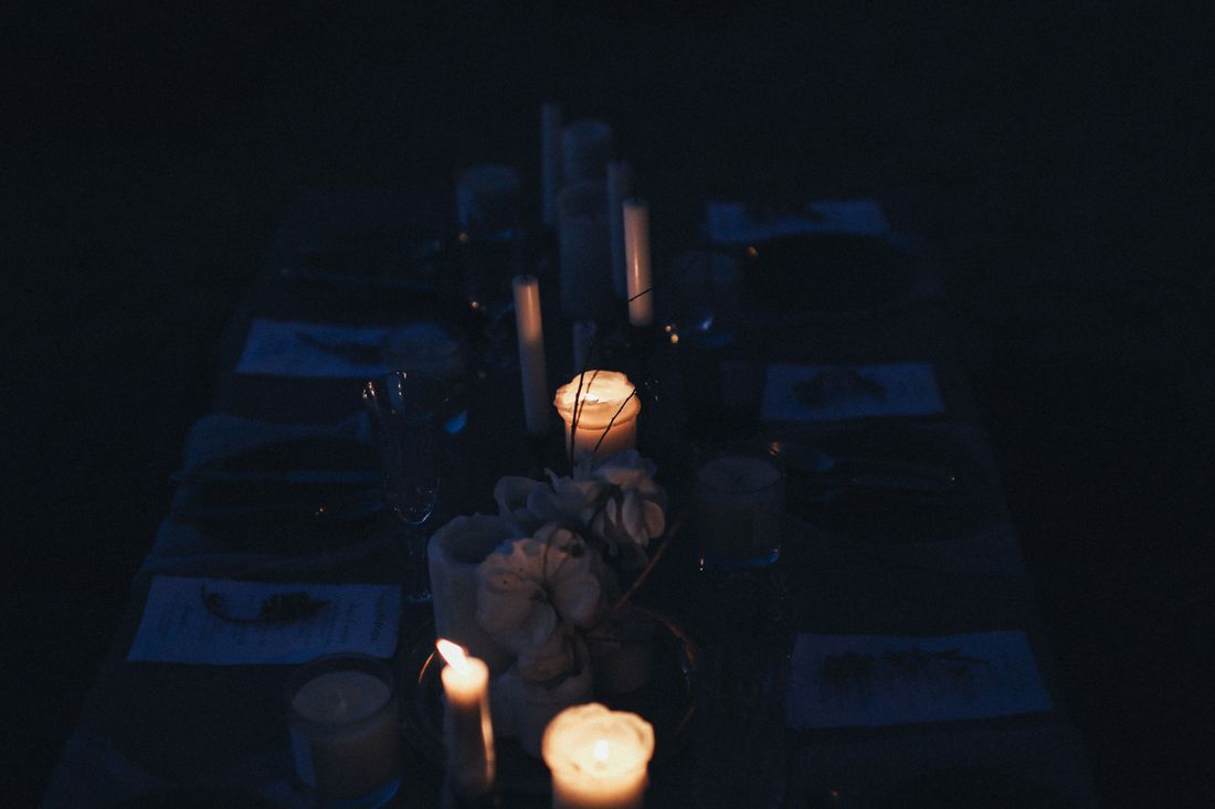 A candlelit dinner table set in a dim room, showing warm low light across glassware and place settings