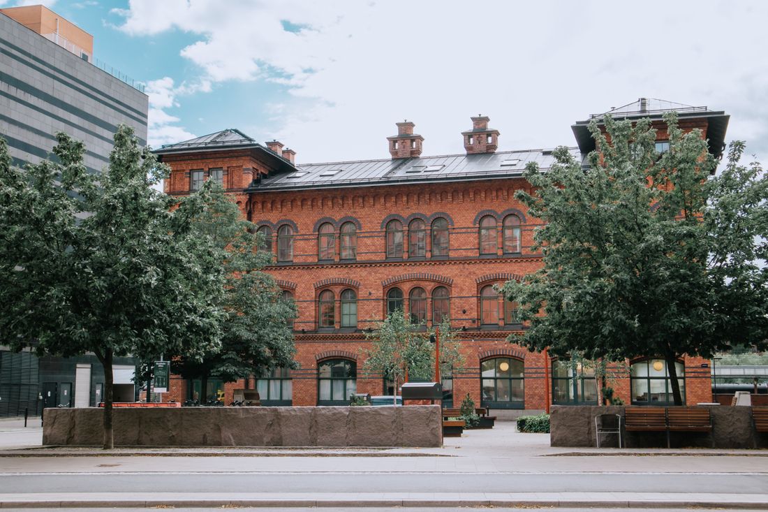 A historic red-brick building with arched ground-floor windows and doorways along a quiet city street, framed by trees