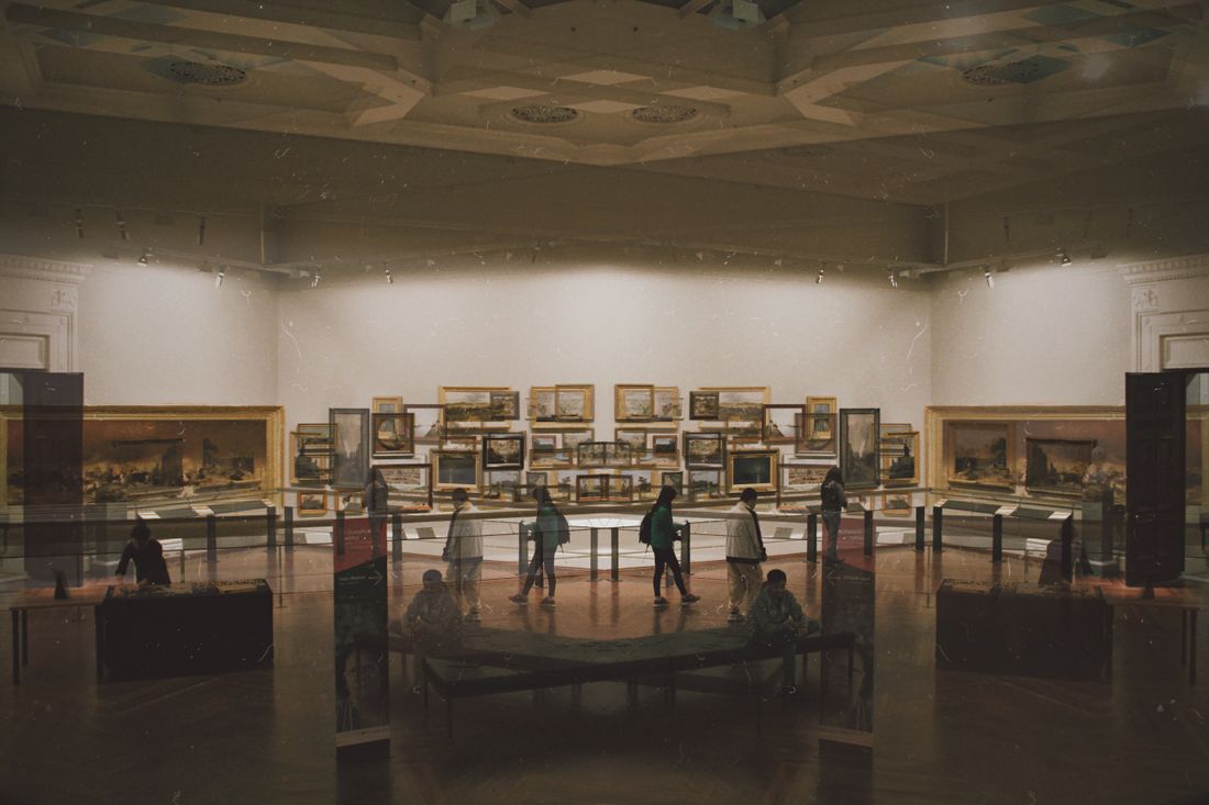 A quiet museum room with display cases down the centre and paintings hung along the walls