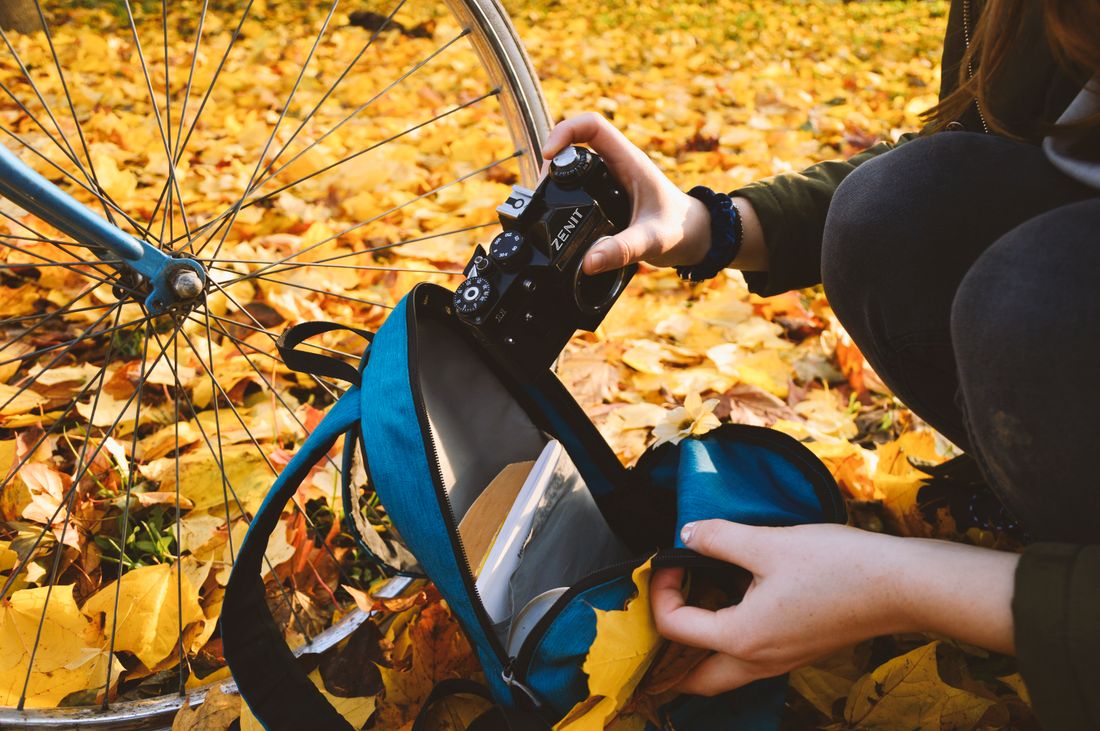 Hands packing a DSLR camera into a bag next to a bicycle, moving quickly between two bookings
