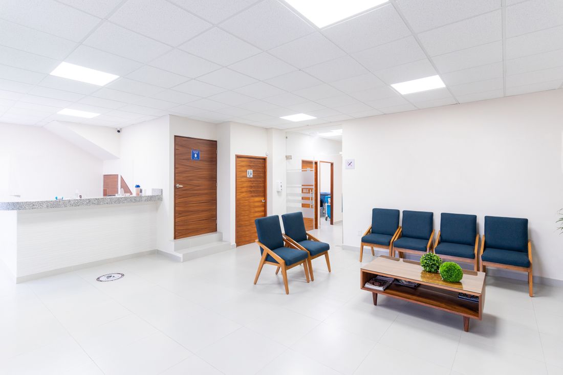 A quiet, clean office waiting area with blue chairs, a reception counter, and no people present.