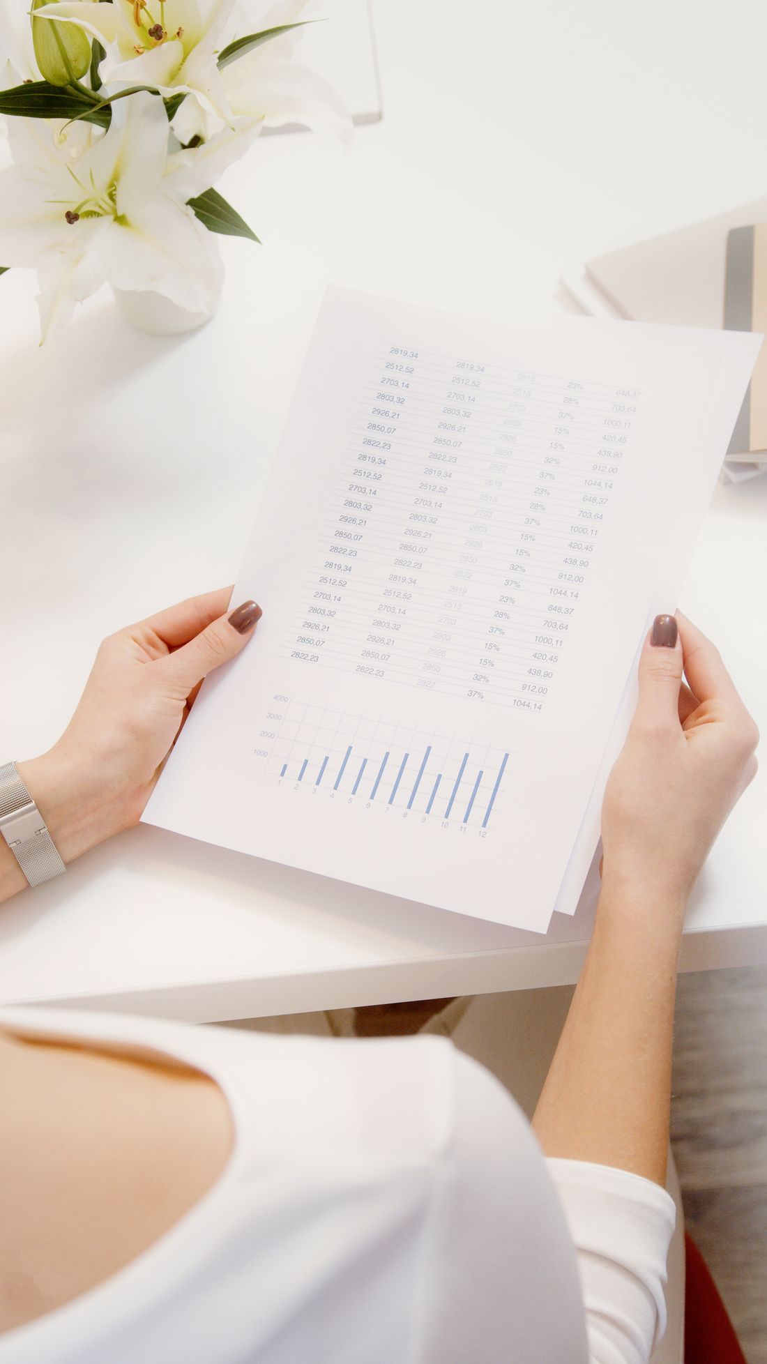 Close-up of hands holding a printed page of financial figures and a small chart on a desk.