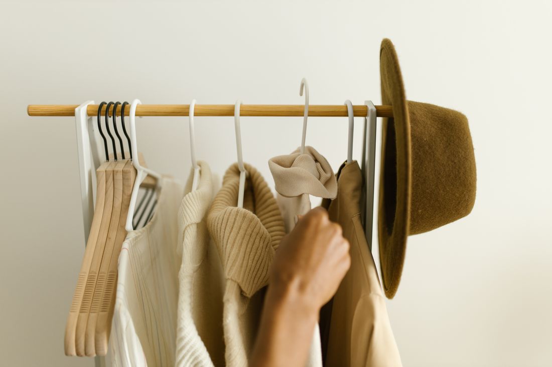A hand reaching into a rack of beige and brown hanging clothes