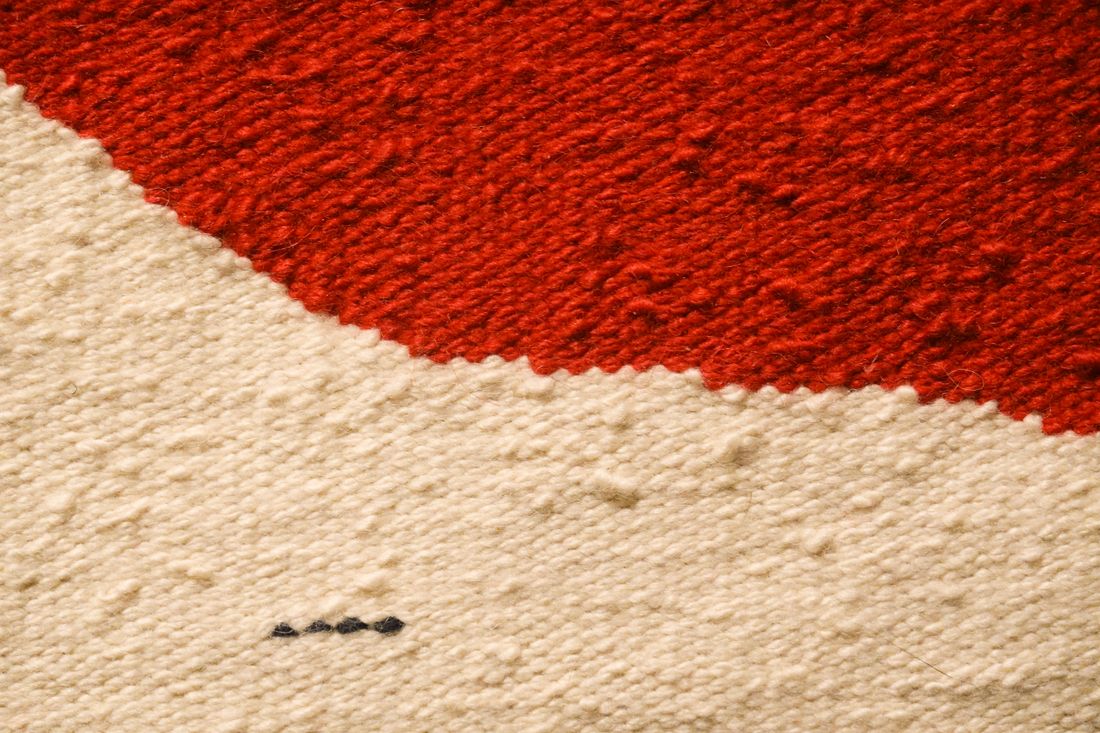 Close-up macro view of red and beige woven wool fabric showing individual thread texture and weave structure
