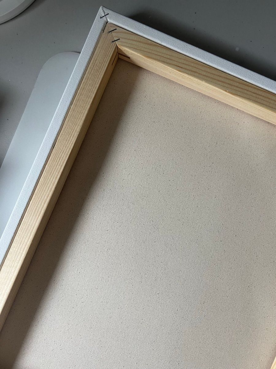 Close-up of the corner of a blank stretched canvas showing the wooden stretcher bar and staples.