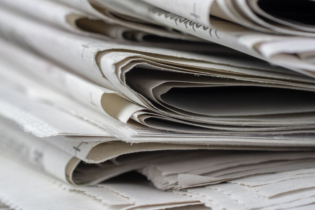 A close-up stack of folded newspapers seen edge-on, their pages fanned out and creased