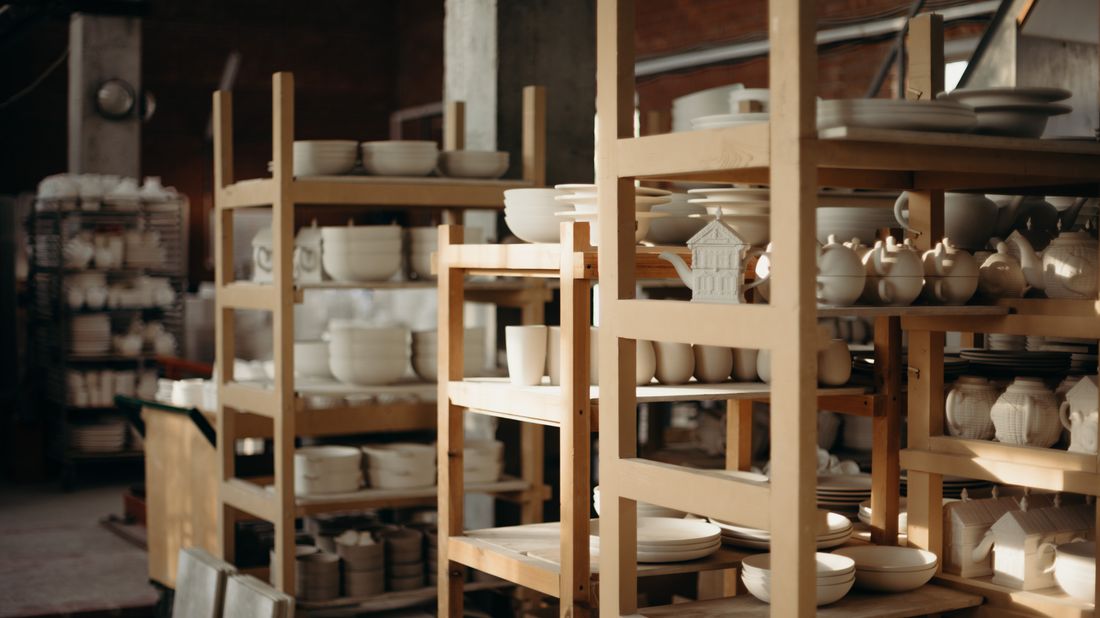 Wooden shelving stacked with unglazed ceramic pieces in an organized, quiet workshop, no people in frame.