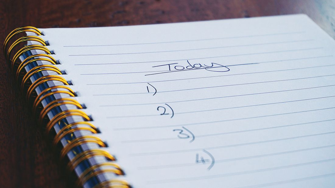 A handwritten numbered to-do list in a spiral notebook on a wooden desk