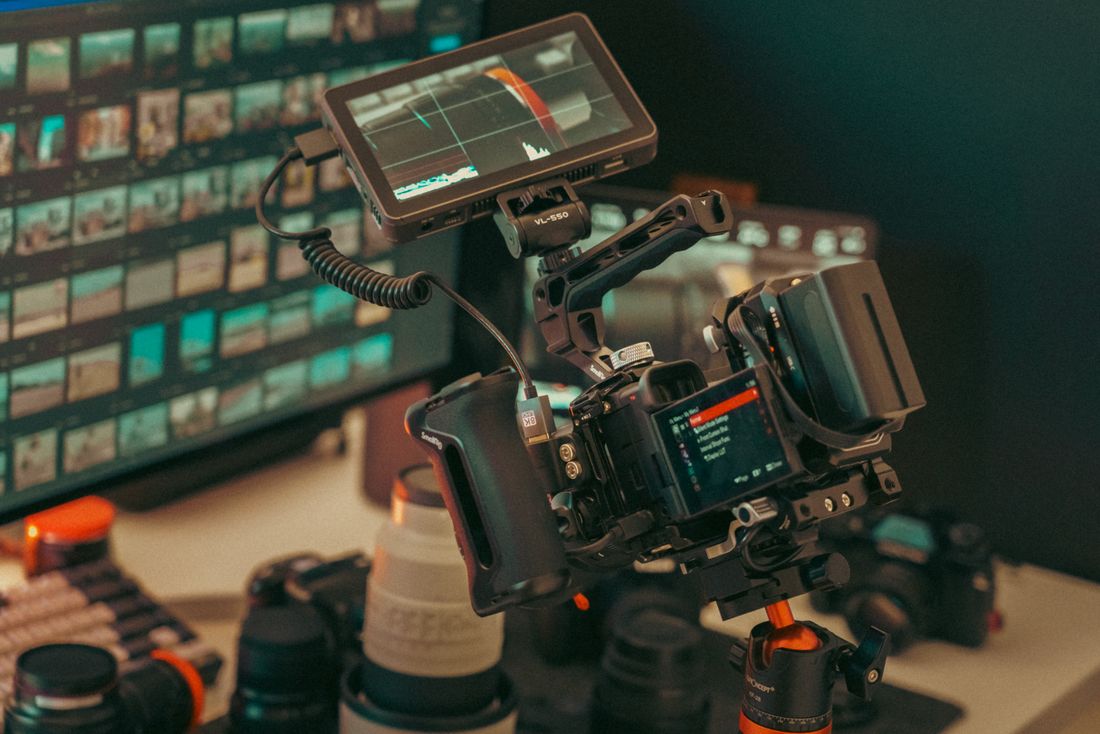A small on-location video production setup with a camera, external monitor, and lenses on a desk
