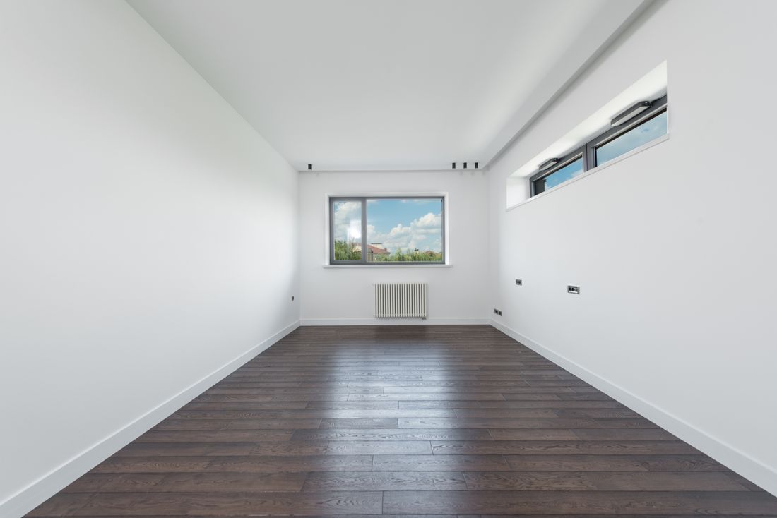 Empty room with bare white walls, dark wood flooring, and daylight coming through a window, with no furniture or people.