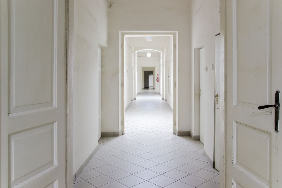 Open double doors leading into a bare white hallway lit by daylight, with no people in view.
