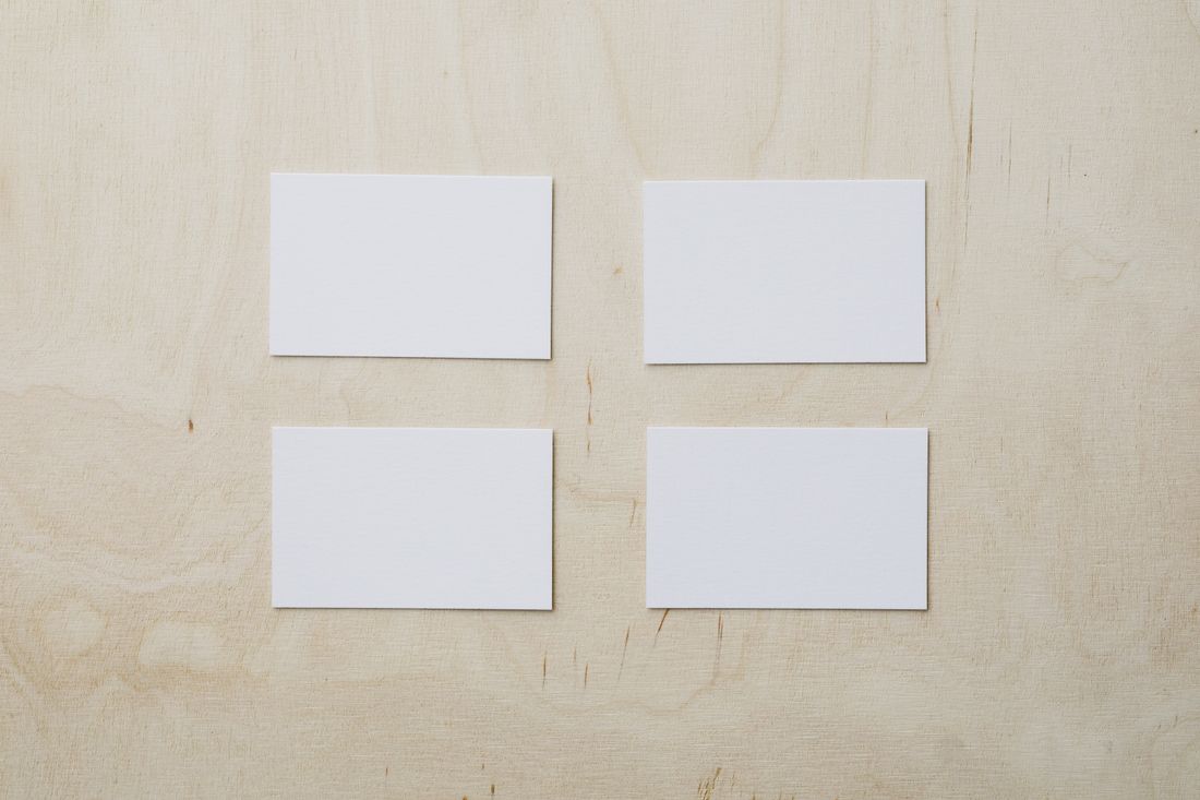 Four blank white cards laid out in a grid on a plain plywood surface, seen from directly above.