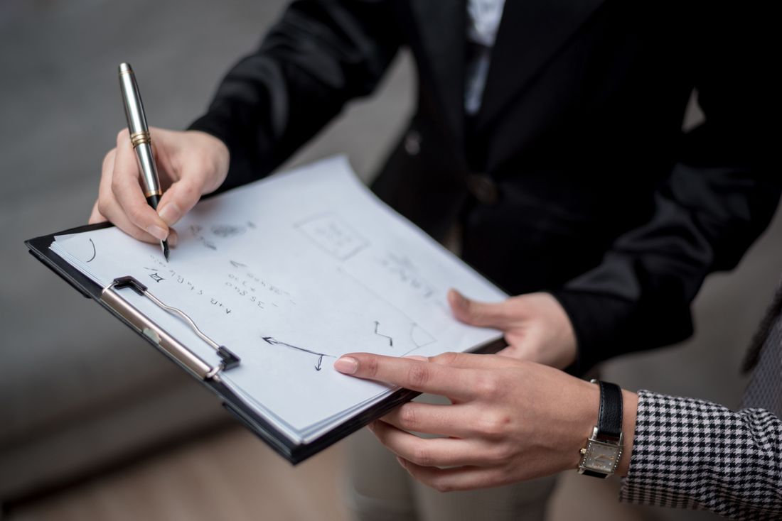 A close view of hands writing on a clipboard with a simple diagram sketched on it